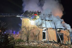 Zerstörtes Wohnhaus nach Explosion, Feuerwehr im Einsatz, Flammen und Trümmer sichtbar.