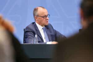 Friedrich Merz steht im Mittelpunkt, begleitet von politischen Symbolen und einem kritischen Atmosphären-Hintergrund.