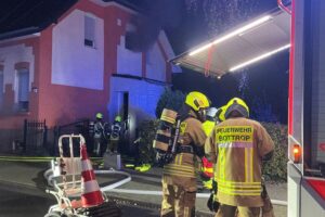 Feuerwehr im Einsatz bei Wohnungsbrand in Doppelhaushälfte, Rauch und Rettungsmaßnahmen sichtbar.