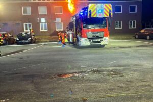 Drehleiter der Feuerwehr im Einsatz gegen Zimmerbrand, Flammen schlagen aus Fenster.