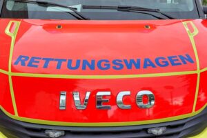 Rettungswagen vor einem Unfallort, Polizisten sichern die Kreuzung, verletzter Fußgänger im Krankenhaus.