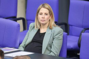 Verena Hubertz, Bundesbauministerin, steht im Bundestag, schwanger und selbstbewusst, diskutiert Herausforderungen.