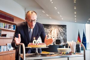 Friedrich Merz pustet Kerzen auf Geburtstagstorte, umgeben von Mitarbeitern im Kanzlerbüro.