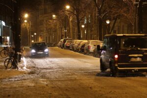 Schneebedeckte Straße mit gepflegtem Winterdienst-Fahrzeug und Streusalzbehältern im Hintergrund.