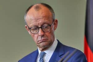 Friedrich Merz steht auf einer Pressekonferenz, umgeben von Journalisten und Kameras, besorgt.