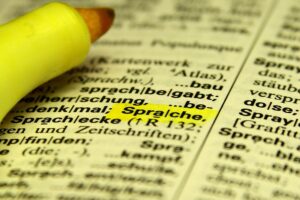 Fünf Schülerinnen stolz mit Urkunden, umgeben von Wörterbüchern und Symbolen für Mehrsprachigkeit.
