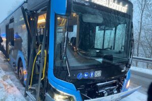 Ein beschädigter Schulbus auf winterlicher Straße, abgesichert durch die Polizei, nach Unfall.