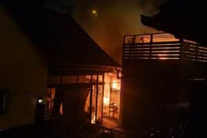 Ein brennendes Gartenhaus mit Feuer und Rauch, Feuerwehr im Einsatz, Verletzter wird gerettet.
