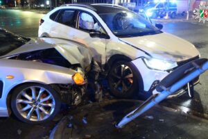Kreuzung nach Verkehrsunfall gesperrt, beschädigte Fahrzeuge und Verkehrszeichen sichtbar. Polizei vor Ort.