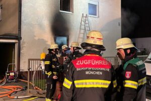 Feuerwehr München rettet verletzten Mann aus brennendem Mehrfamilienhaus, Lösch- und Rettungseinsatz im Gange.