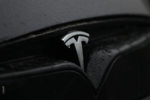 Elon Musk mit Tesla-Auto, symbolisiert Aktionärszustimmung für milliardenschweres Vergütungspaket.