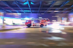 Feuerwehr im Einsatz am Bahnübergang nach Bahnunfall, Rettungsarbeiten und evakuierte Fahrgäste sichtbar.