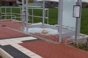 Zerstörtes Buswartehäuschen mit zerbrochenem Glas in einer urbanen Umgebung.