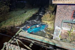 Verunfallter BMW liegt im Fluss nach illegalem Autorennen; Polizei und Feuerwehr im Einsatz.