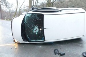 Unfallfahrzeug auf der Seite, Einsatzkräfte sichern Unfallstelle und helfen verletzter Fahrerin.
