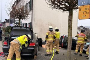 Unfallstelle mit beschädigtem BMW, Hauswand und Absperrung durch Feuerwehr und Polizei.