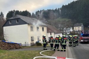 Ein beschädigtes Einfamilienhaus nach Brand, mit Feuerwehr und Polizei im Einsatz.