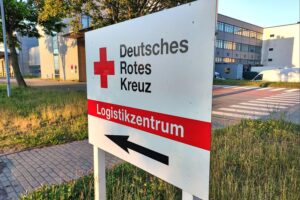 Ein Bild des DRK-Logistikzentrums mit ehrenamtlichen Helfern und Hilfsgütern.
