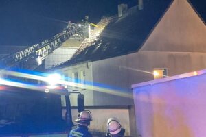 Drehleiter der Feuerwehr entfernt Dachteile bei Nacht, um Feuer in Wohnung zu löschen.