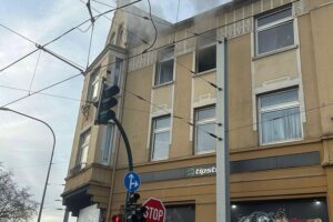 Küchenbrand in Mehrfamilienhaus, Feuerwehr im Einsatz, Anwohner evakuiert, Rauchentwicklung sichtbar.