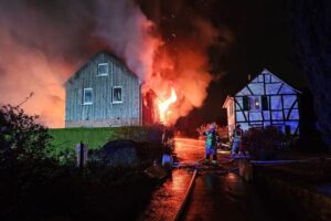 Ein Fachwerkhaus brennt lichterloh, Feuerwehrleute kämpfen gegen die Flammen, Rauch quer über den Himmel.
