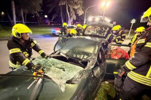 Feuerwehr befreit verletzte Fahrerin nach Alleinunfall, beschädigter Laternenmast im Hintergrund sichtbar.