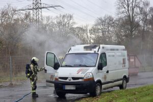Feuerwehr löscht brennenden Kleinbus; Einsatzkräfte bei Brandbekämpfung und Sicherheitsüberprüfung.