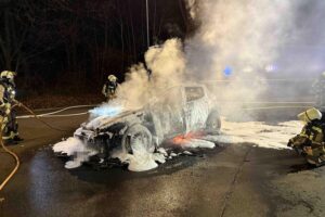 Feuerwehr löscht brennenden Pkw auf Rastplatz, Einsatzkräfte kontrollieren Umgebung, keine Verletzten.
