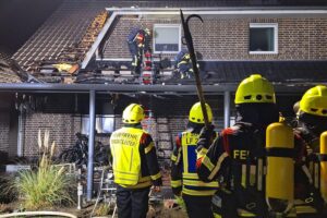 Feuerwehr löscht Brand an Doppelhaus, Zuschauer stehen bereit, Einsatzkräfte arbeiten fokussiert.