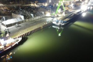 Löschboot im Einsatz am Hafen, um ein beschädigtes Frachtschiff zu unterstützen.
