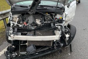 Zwei beschädigte Autos auf Straße, Polizei und Feuerwehr sichern Unfallort bei Regenwetter.