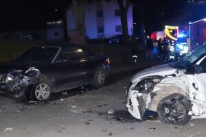Zwei stark beschädigte Autos nach frontalem Unfall auf Kreisstraße, Polizei am Einsatzort.