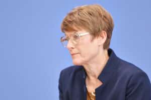 Ein Porträt von Veronika Grimm mit ernstem Ausdruck, Hintergrund in einem politischen Kontext.