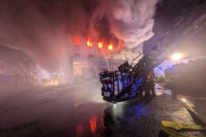 Feuerwehrkräfte bekämpfen großen Brand in Gewerbeobjekt, dichter Rauch aufsteigend aus dem Obergeschoss.