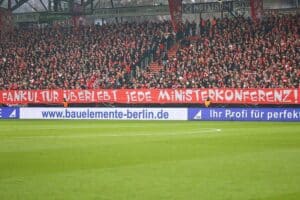 Protestierende Fußballfans, Banner gegen Sicherheitsverschärfungen, Stimmung der Solidarität und Zusammenhalt.