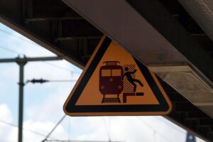 Warnschild am Bahnhof mit Gefahrenhinweis, um Jugendliche vor Stürzen in Gleisbereich zu schützen.