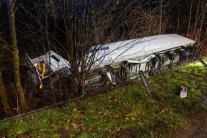 Ein umgestürzter LKW in der Böschung, Feuerwehrleute sichern die Unfallstelle, Verletzte werden versorgt.