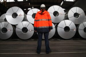 Stahlproduktionsszenario mit Arbeitern, Maschinen und einem backdrop aus Industrieanlagen – symbolisiert Arbeitsplatzabbau.