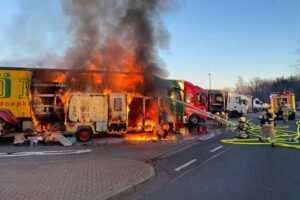 Feuerwehr löscht Transporterbrand auf Autobahn, bedrohliche Flammen und Rauchwolken, winterliche Bedingungen.