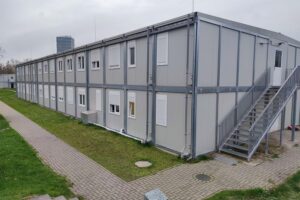 Asylunterkunft mit Menschenschlangen und Behörden, Symbol für aktuelle Migrationspolitiken und Menschenrechtsdiskussionen.