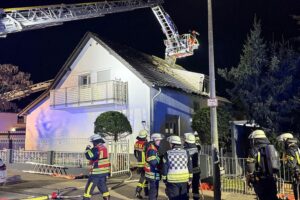 Drehleitern bekämpfen Nachtbrand in Mehrfamilienhaus, Feuerwehr rettet Bewohner, darunter Schwerverletzter.