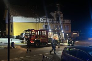 Einsatzkräfte löschen Brand in Mehrfamilienhaus, evakuierte Bewohner, schwarzer Rauch sichtbar.