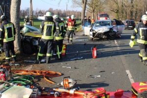 Zwei beschädigte Autos, Einsatzfahrzeuge und Rettungskräfte an Unfallstelle mit Verletzten.