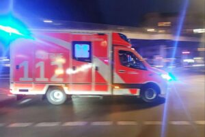 Rettungswagen am Unfallort mit beschädigten Fahrzeugen und blauen Blinklichtern im Hintergrund.