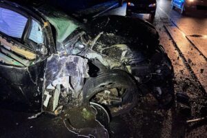 Ein schwer beschädigter BMW nach einem Verkehrsunfall, Rettungskräfte und Polizei vor Ort.