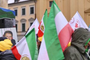 Iranische Flaggen vor einer unruhigen politischen Kulisse, Symbol für aktuelle Abschiebungsdebatten.