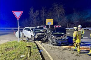 Zwei stark beschädigte Fahrzeuge nach Verkehrsunfall, Feuerwehr und Rettungsdienst betreuen Verletzte.