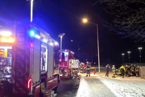 Rettungseinsatz der Feuerwehr: Patient wird aus Unfallfahrzeug befreit, beschädigte Laterne im Hintergrund.