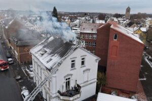 Feuerwehr löscht Kaminbrand in Mehrfamilienhaus; Einsatzkräfte, Drehleiter und Rauchentwicklung sichtbar.
