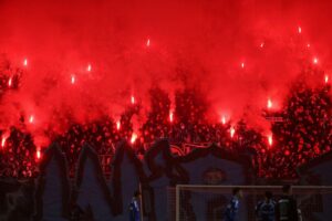 Fußball-Fans zünden Pyrotechnik; im Hintergrund Polizeikräfte während Ausschreitungen in Magdeburg.
